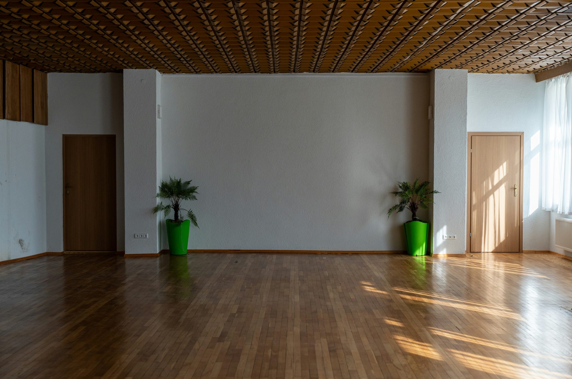 Una habitación grande con suelo de madera y dos jarrones verdes.
